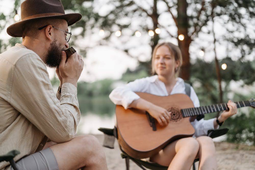 A man with a harmonica and a woman with a guitar playing music together in a natural setting.